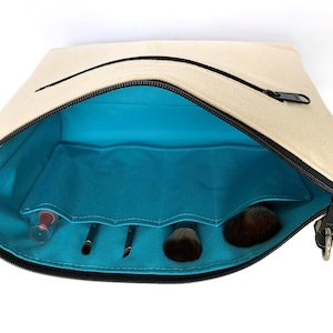 May include: A beige canvas makeup bag with a black zipper and a turquoise lining. The bag is open and has several compartments for makeup brushes and other items.
