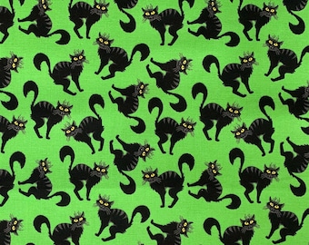 May include: A green fabric with a repeating pattern of black cats in various poses. The cats have yellow eyes and are outlined in black.