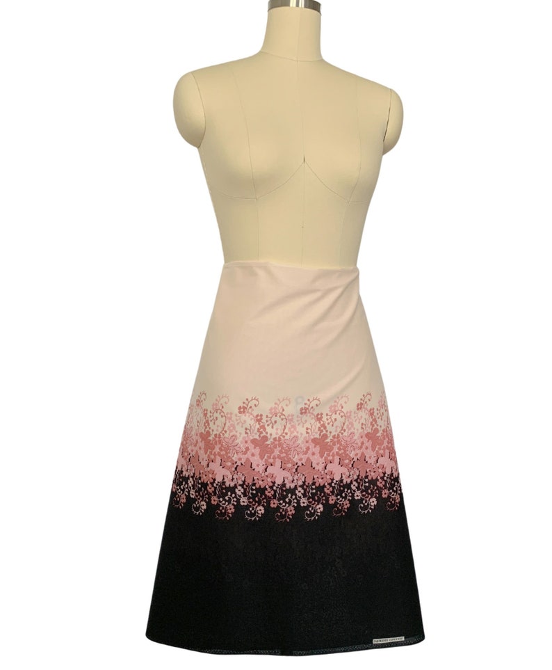 May include: A pink and black A-line skirt with a floral print. The skirt has a gradient pattern with pink flowers on a white background that fades to black at the bottom.