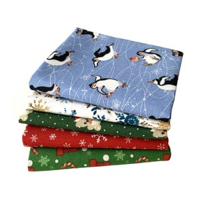 May include: A stack of six fabric squares with different Christmas-themed patterns. The top square is light blue with white snowflakes and penguins. The other squares feature snowflakes, candy canes, and a polar bear.