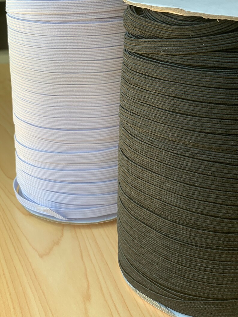 May include: Two spools of elastic ribbon. One spool is white, and the other is dark brown. The elastic is tightly wound on cardboard spools. The elastic is likely used for sewing or crafting projects.