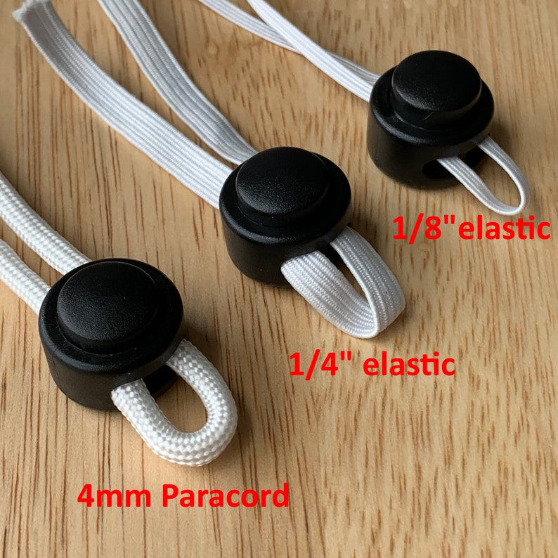 May include: Three black plastic toggles with white elastic cord and 4mm paracord. The elastic cords are labeled 1/8" elastic, 1/4" elastic, and 4mm paracord.