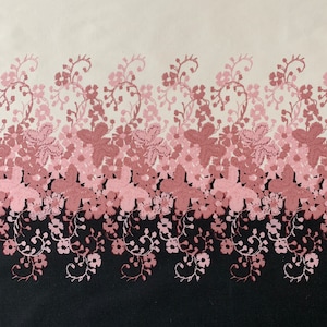 May include: A white fabric with a pink floral pattern. The floral pattern is a repeating design of pink flowers and vines. The fabric has a black background at the bottom.