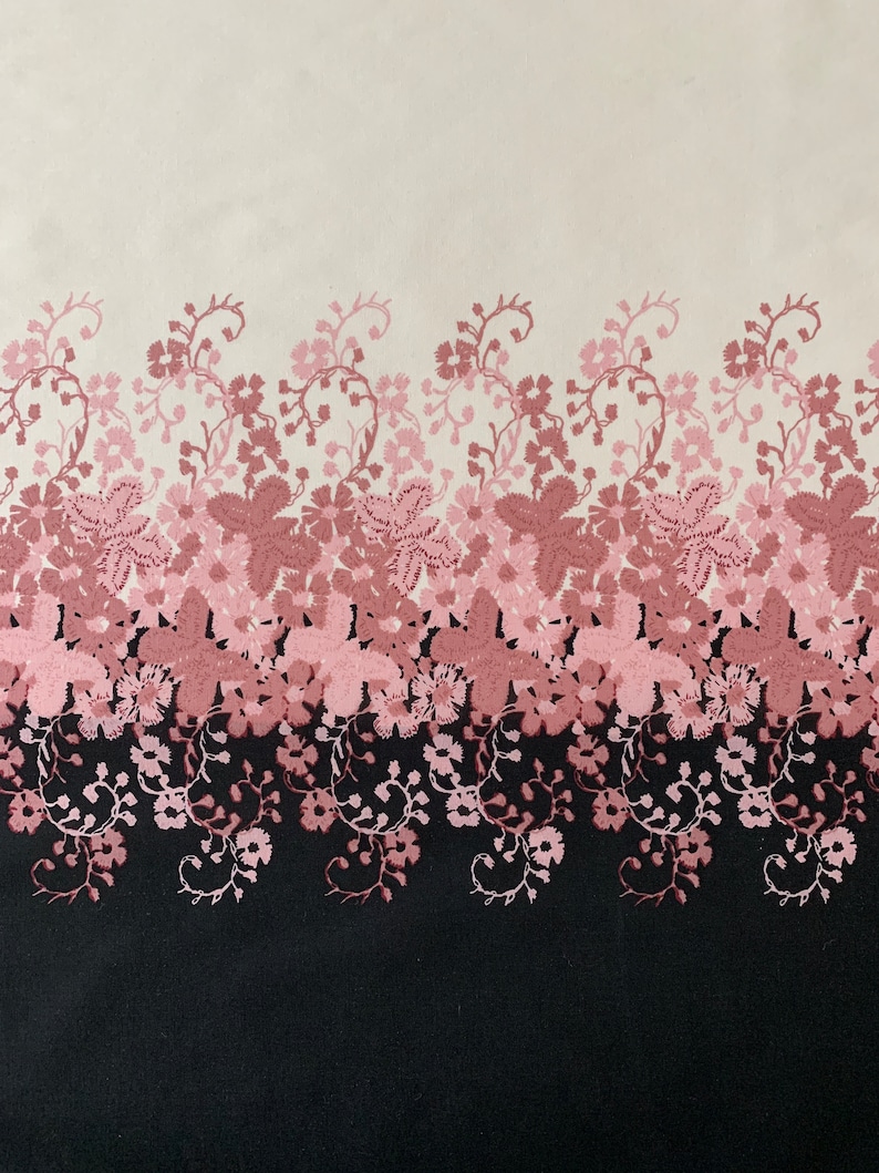 May include: A white fabric with a pink floral pattern. The floral pattern is a repeating design of pink flowers and vines. The fabric has a black background at the bottom.