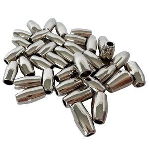 May include: A pile of shiny, silver-colored barrel-shaped beads. Each bead has a smooth, metallic finish and a cylindrical shape with a hole at each end. The beads are scattered, creating a textured surface.
