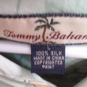 May include: A light green silk shirt with a palm tree print and the text "Tommy Bahama" on the label. The label also states "100% Silk, Made in China, Copyrighted Print".