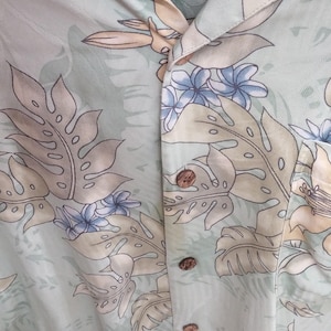May include: A light green silk button-down shirt with a tropical print featuring palm trees, flowers, and leaves. The shirt has a Tommy Bahama label and is made in China.