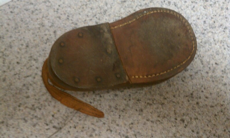 May include: The underside of a brown leather shoe with a stitched seam and a leather strap. The shoe has several metal rivets.