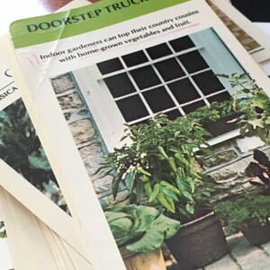 May include: A close-up of a card with the text "DOORSTEP TRUCK FARM" and the caption "Indoor gardeners can top their country cousins with home-grown vegetables and fruit." The card features a photo of a window with plants growing in pots on a stone ledge.