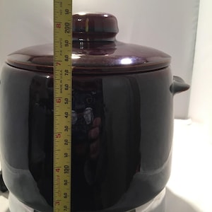May include: A dark brown ceramic pot with a lid. The pot has two handles and is approximately 8 inches tall. The pot is made in the USA.