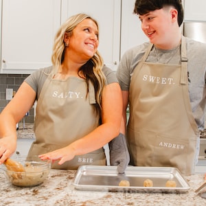 A man and woman in the kitchen wearing beige aprons and making cookies