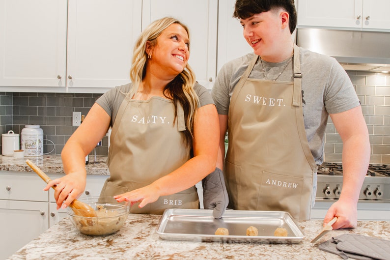 A man and woman in the kitchen wearing beige aprons and making cookies