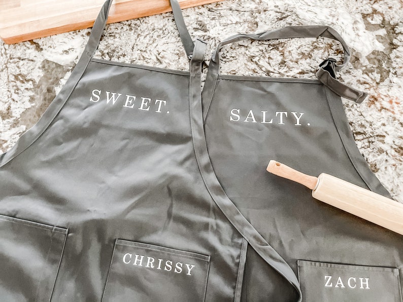 Two grey aprons on a granite counter with a rolling pin.