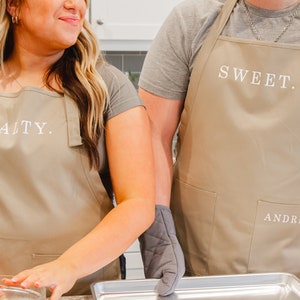 A man and woman in the kitchen wearing beige aprons and making cookies