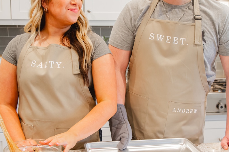 A man and woman in the kitchen wearing beige aprons and making cookies