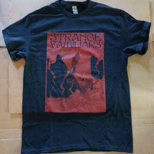May include: A black t-shirt with a red graphic print of a bird with the text "STRANGE FAMILIARS" in black.