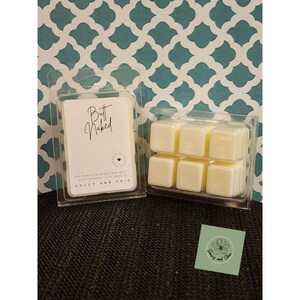 May include: Two clear plastic packages of soy wax melts. One package has a label that reads "Butt Naked" in script. The other package contains six square wax melts. A small sticker with a floral design is in the bottom right corner.