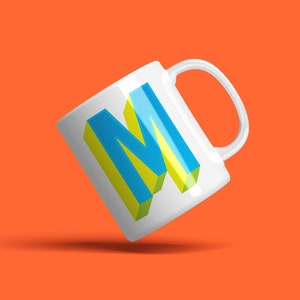 May include: White ceramic mug with a 3D blue and yellow letter "M" printed on the front.