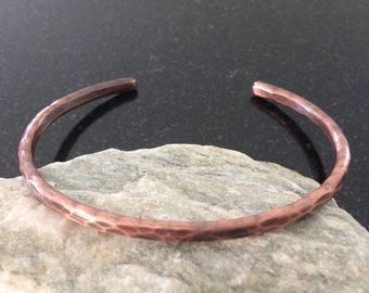 May include: A hammered copper bangle bracelet. The bracelet is a simple, minimalist design with a smooth, polished finish.