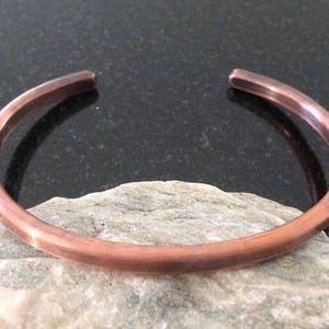 May include: A simple copper bangle bracelet. The bracelet is smooth and has a polished finish.
