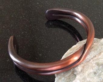 May include: A copper bracelet with a twisted design. The bracelet is made of a single piece of metal that has been bent and twisted to create a unique and stylish look.