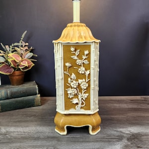 May include: A ceramic table lamp with a yellow and white base. The base is decorated with a floral design and bamboo stalks. The lamp is in a vintage style.