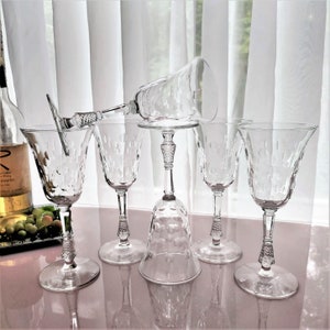 May include: Set of six clear glass wine glasses with a textured design. The glasses have a tall, slender stem and a wide bowl. The glasses are arranged on a table with a white tablecloth.