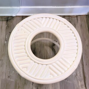 May include: White round table with a woven design and a circular opening in the center. The table is made of white wicker.