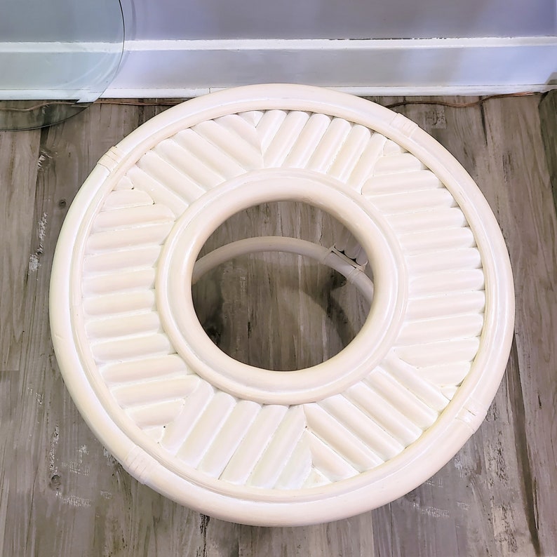 May include: White round table with a woven design and a circular opening in the center. The table is made of white wicker.