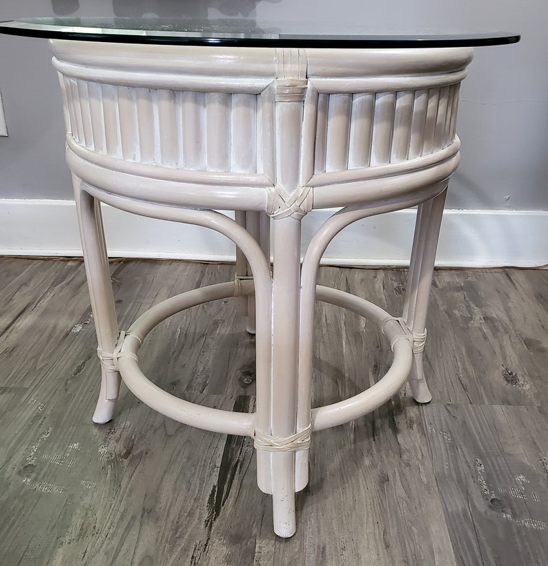 May include: White wicker end table with a round glass top. The table has a woven design and a simple, elegant style.