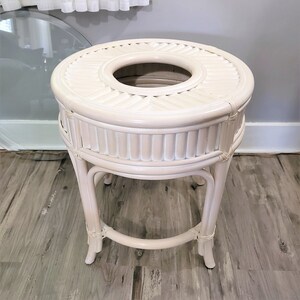 May include: White wicker plant stand with a round top and three legs. The top has a circular opening in the center.