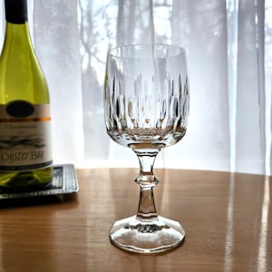 May include: A clear glass wine glass with a tall, slender stem and a wide bowl. The bowl has a decorative, faceted design.