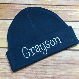 May include: A dark blue knitted beanie with the name "Grayson" embroidered in white on the front.