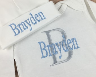 Può includere: Un body bianco per neonato e un cappello abbinato con il nome "Brayden" ricamato in blu su entrambi gli articoli. Il body ha anche una grande "B" argentata con il nome "Brayden" ricamato in blu.