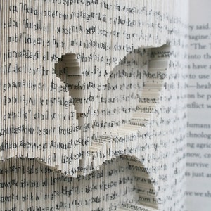 May include: A book with pages folded into a three-dimensional shape, creating a bird in flight. The book is open and the text on the pages is visible. The text reads, "We're on the sagine." "The Transhumanist into the mainstream. I have a moral obliga- to use our technolo -healthier, stronger, on be possible. Conflict with the evolu- humans have evolved technologies along the ng agriculture to feed now, creating genetic survive in a changing is just another step in we should embrace"