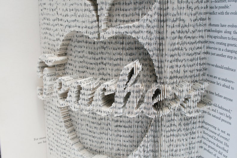 May include: A book with pages folded into a three-dimensional design, creating the word "Embrace" in a white, gray, and black color scheme.