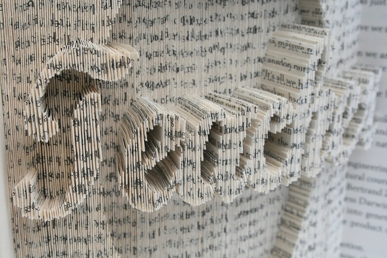 May include: A book art sculpture made from the pages of a book, folded and shaped to create the word "LOVE". The pages are white with black text.