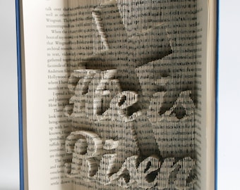 May include: A book with the word "The" and "Dream" cut out of the pages, creating a 3D effect. The pages are folded and layered to create the words.