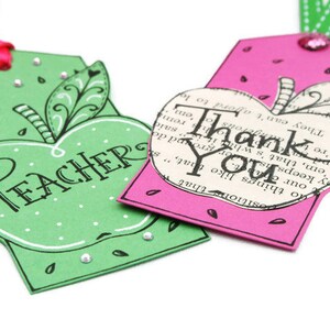 May include: Two apple-shaped gift tags. One is green with white polka dots and the word "TEACHER" in black script. The other is pink with white polka dots and the words "Thank You" in black script.