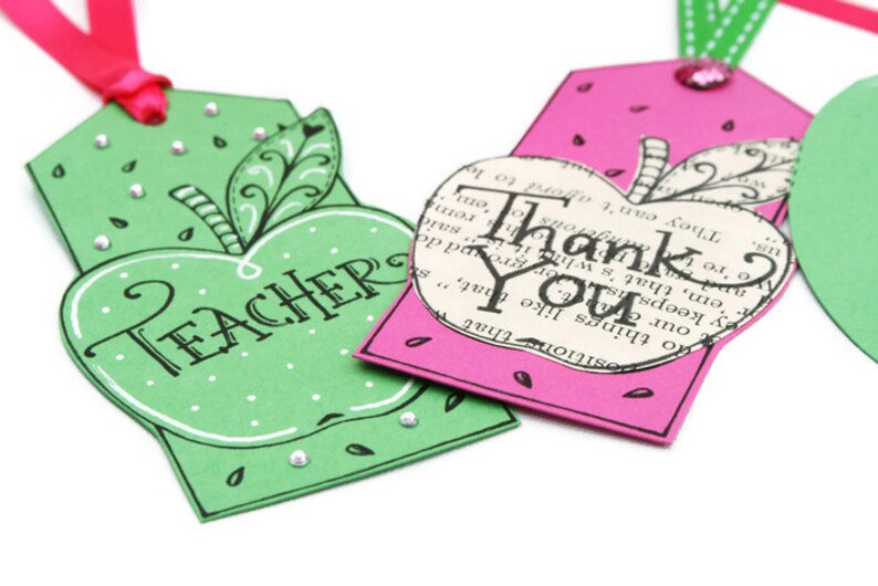 May include: Two apple-shaped gift tags. One is green with white polka dots and the word "TEACHER" in black script. The other is pink with white polka dots and the words "Thank You" in black script.