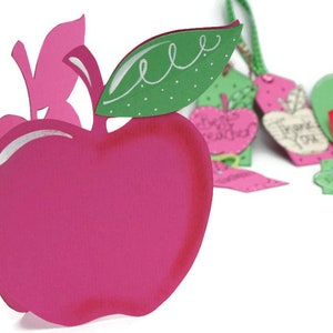 May include: A pink paper apple with a green leaf and white polka dots. The apple is a card or gift tag with a cut-out design.