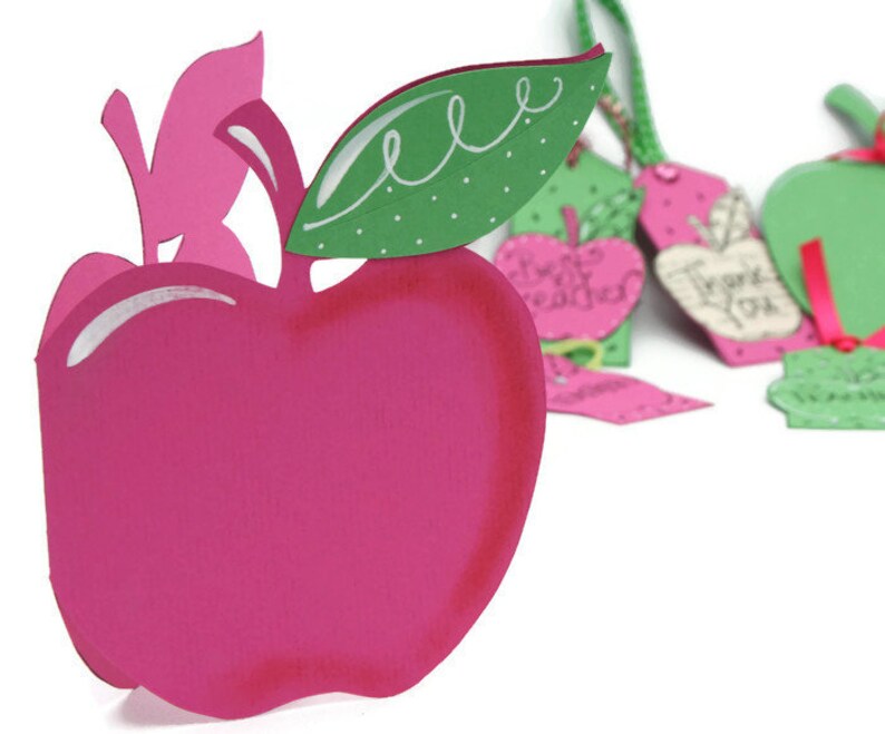 May include: A pink paper apple with a green leaf and white polka dots. The apple is a card or gift tag with a cut-out design.