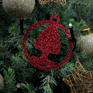 May include: Red glitter Christmas ornament shaped like a tree in a circle. The ornament is hanging on a green Christmas tree.