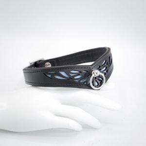 May include: A black leather collar with a blue floral design and a silver ring.