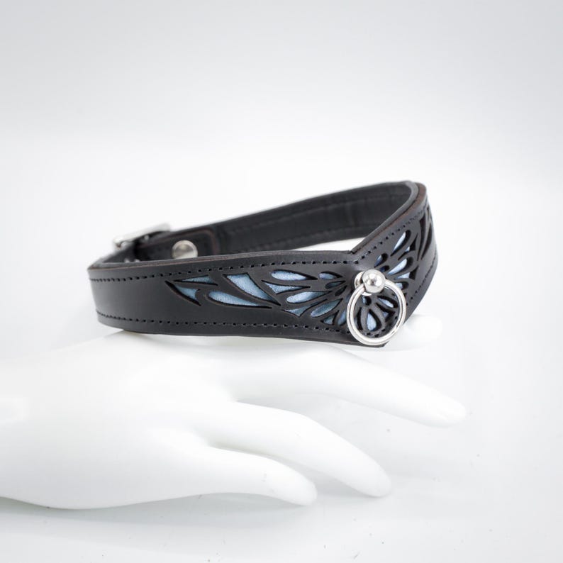 May include: A black leather collar with a blue floral design and a silver ring.