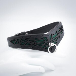K&ouml;nnte beinhalten: Ein schwarzes Lederhalsband mit geometrischem Ausschnitt und gr&uuml;ner Futter. Das Halsband hat einen silbernen Ring mit einer Kugel auf einer Seite.