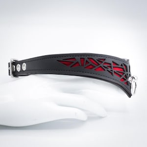 K&ouml;nnte beinhalten: Schwarzes Lederhalsband mit einem roten geometrischen Ausschnitt und silbernen Beschl&auml;gen.