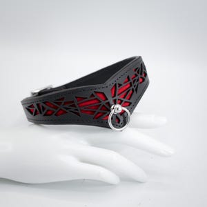 K&ouml;nnte beinhalten: Schwarzer Leder-Choker mit rotem geometrischem Muster und einem silbernen Ring mit einem Kugelakzent.