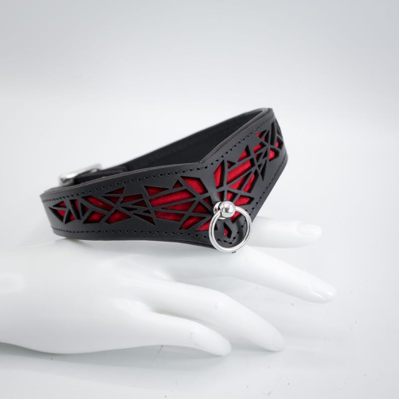 K&ouml;nnte beinhalten: Schwarzer Leder-Choker mit rotem geometrischem Muster und einem silbernen Ring mit einem Kugelakzent.