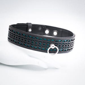Puede incluir: Collar de cuero negro con una incrustación de patrón azul turquesa y un anillo plateado.